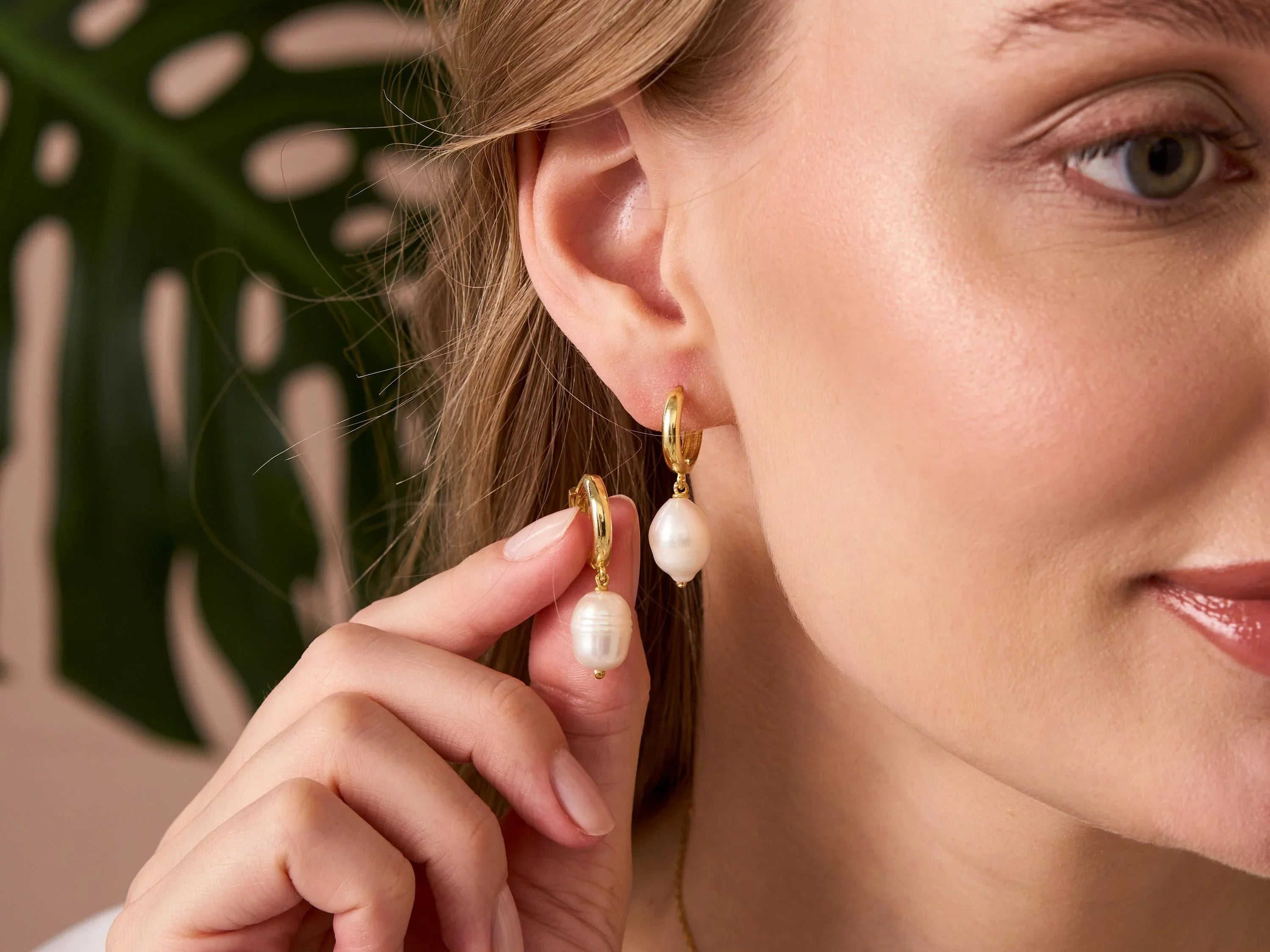 Close-up of a woman wearing pearl earrings with a blurred leaf background