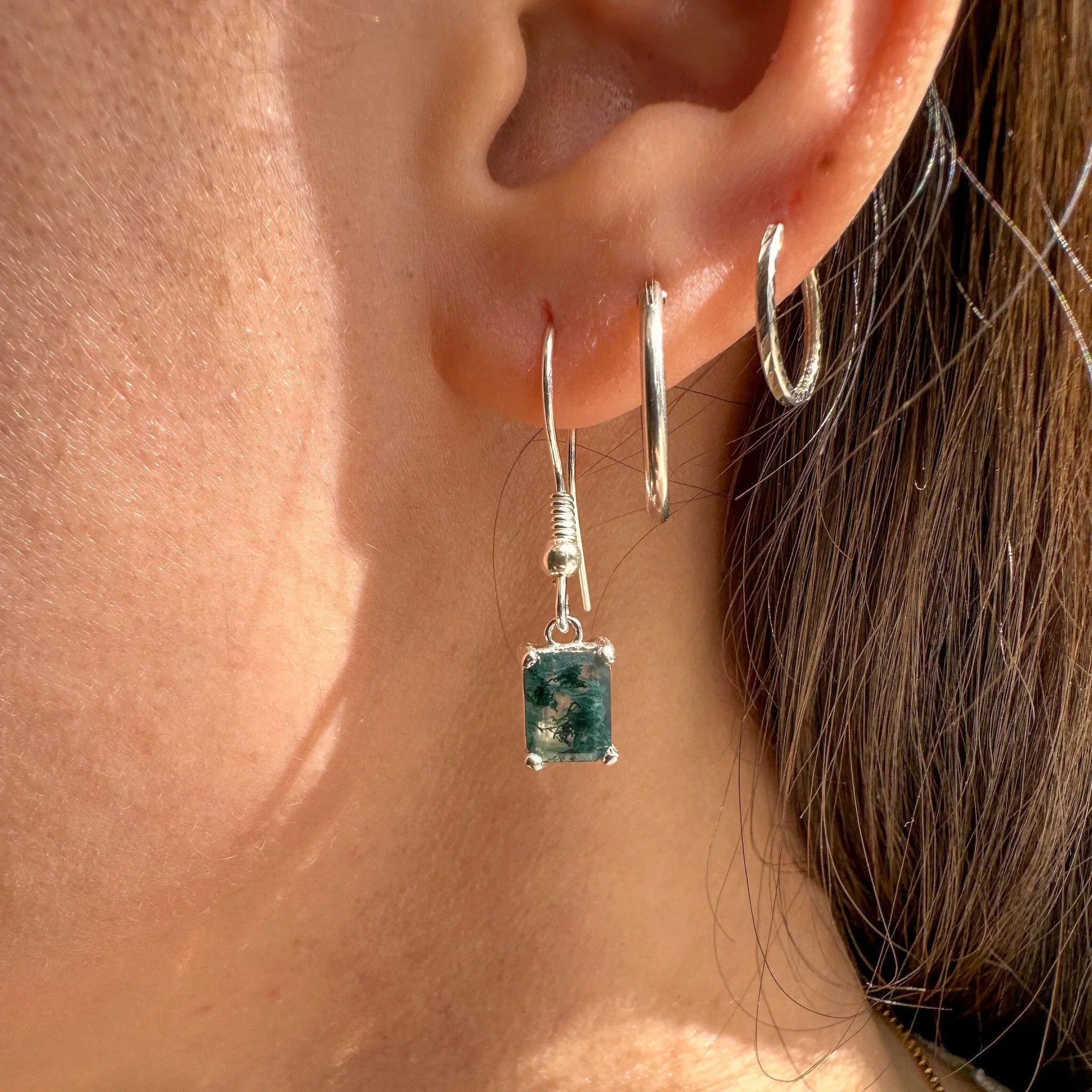Close-up of ear wearing silver hoop and green gemstone drop earring, fine jewelry